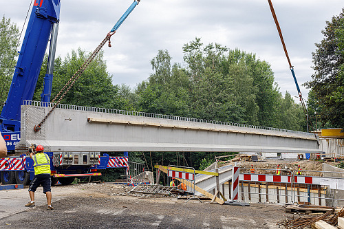 Stavbaři pomocí jeřábu osazují osm železobetonových nosníků. Každý z nich váží...